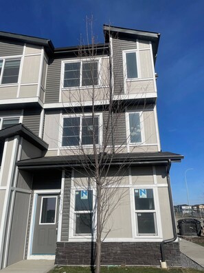 A multi-story residential building with a flat roof, large windows, and a visible tree in front. - Modern Living - Corner Unit Townhome 3 Bedrooms (Calgary)