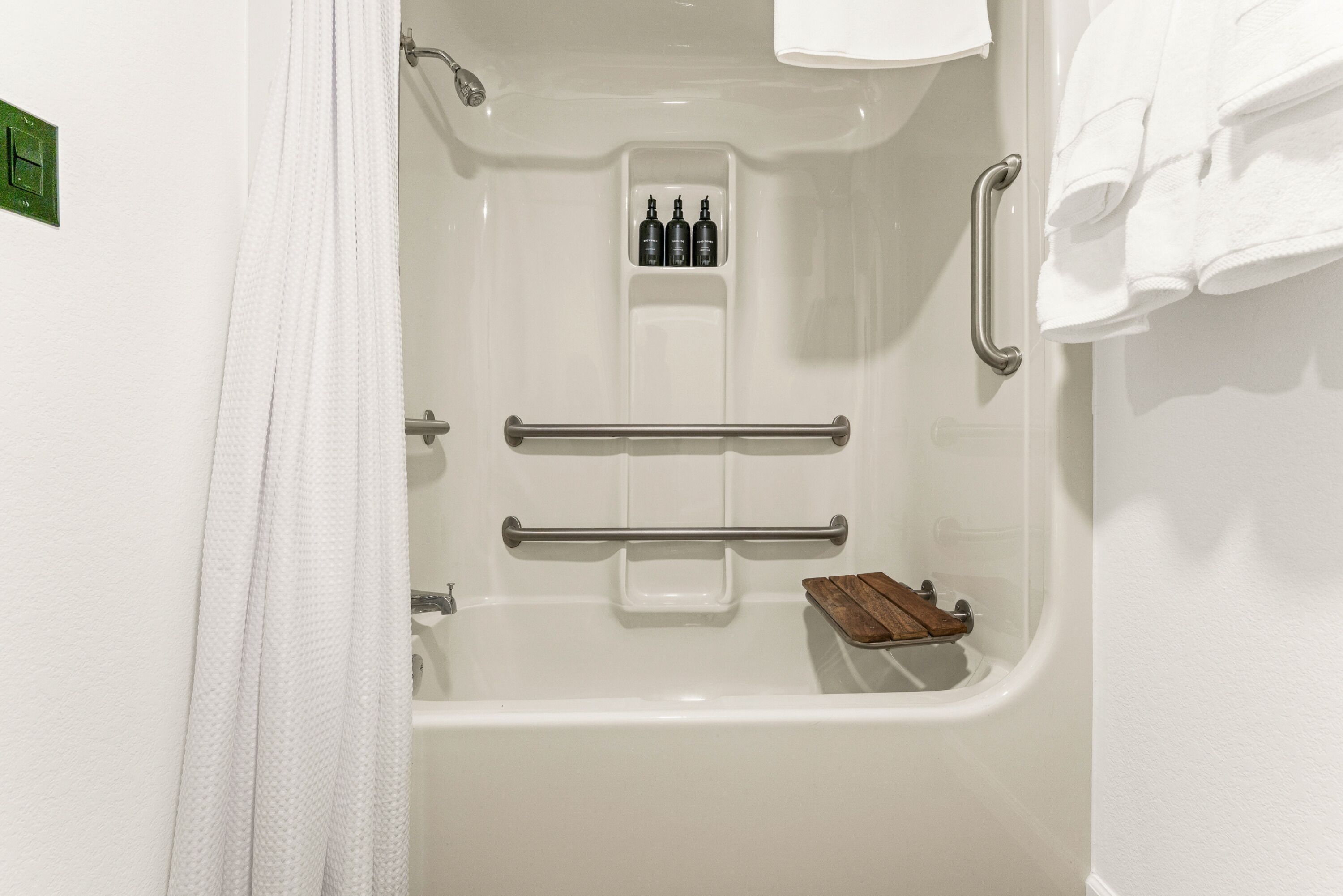 A white bathtub with a wooden tray, a towel rack, and a shelf with bottles.