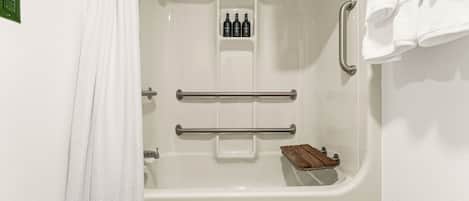 A white bathtub with a wooden tray, a towel rack, and a shelf with bottles.