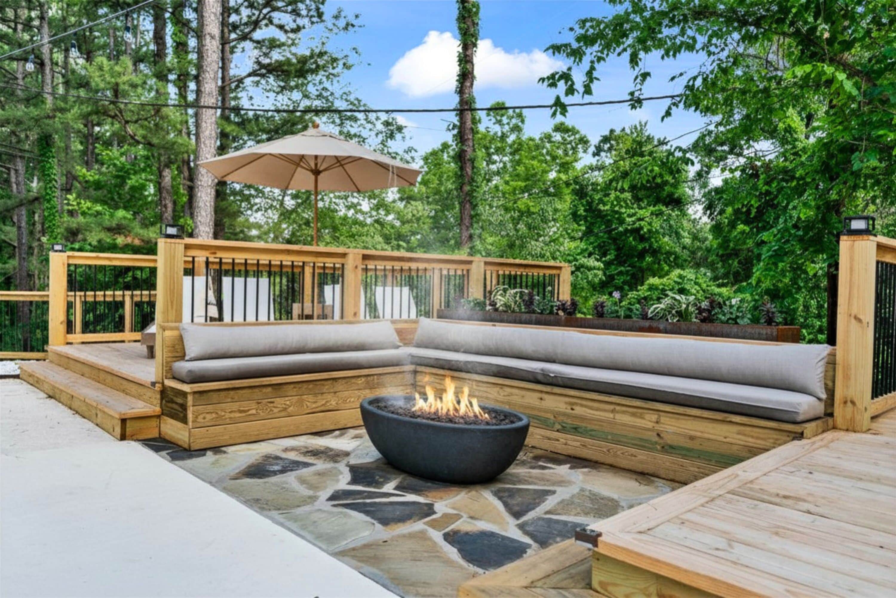 Une terrasse en bois avec un foyer en pierre, un banc rembourré et un parasol.