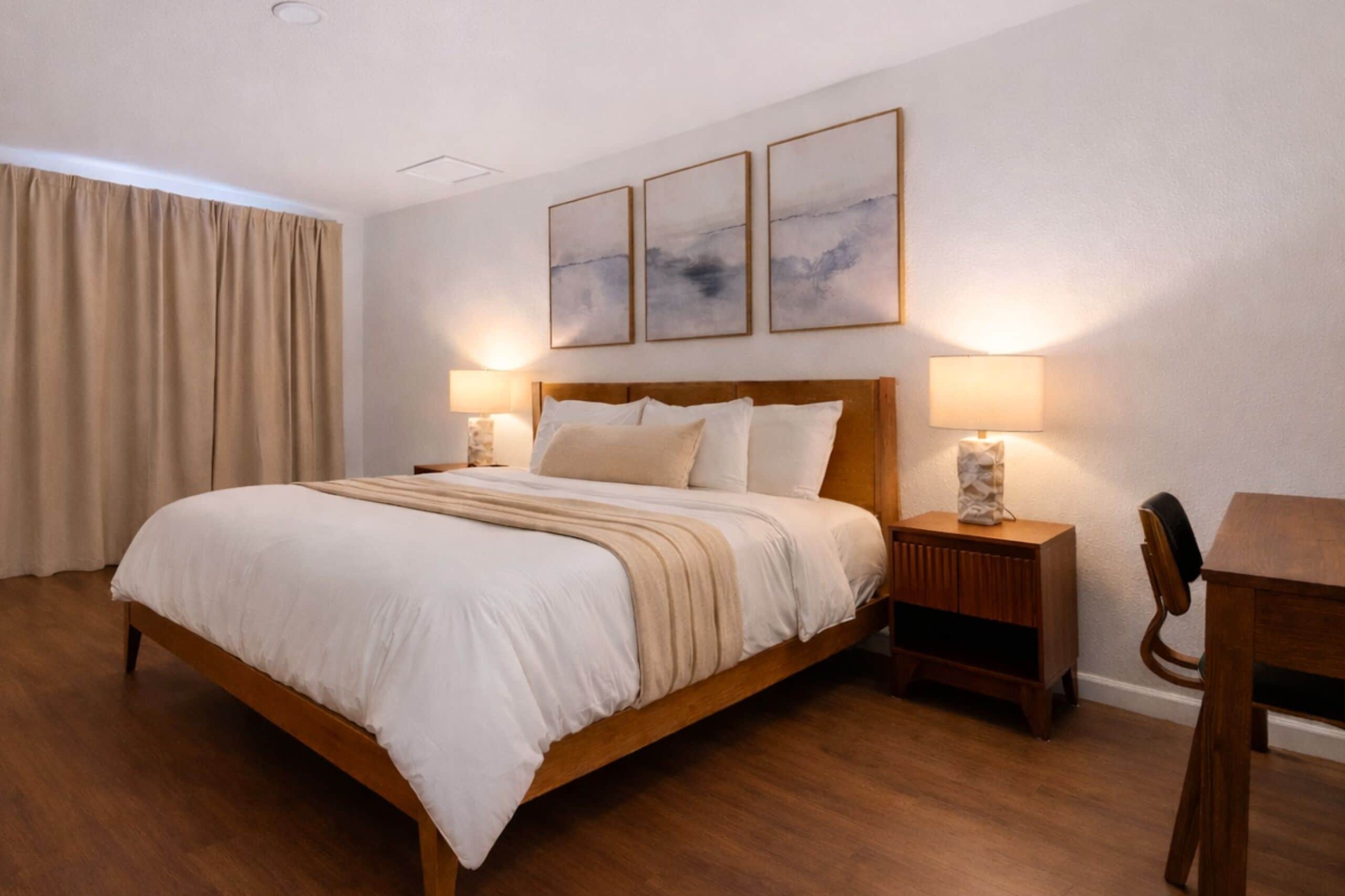 A hotel room with a wooden bed, two bedside tables with lamps, a wooden desk, and a chair.
