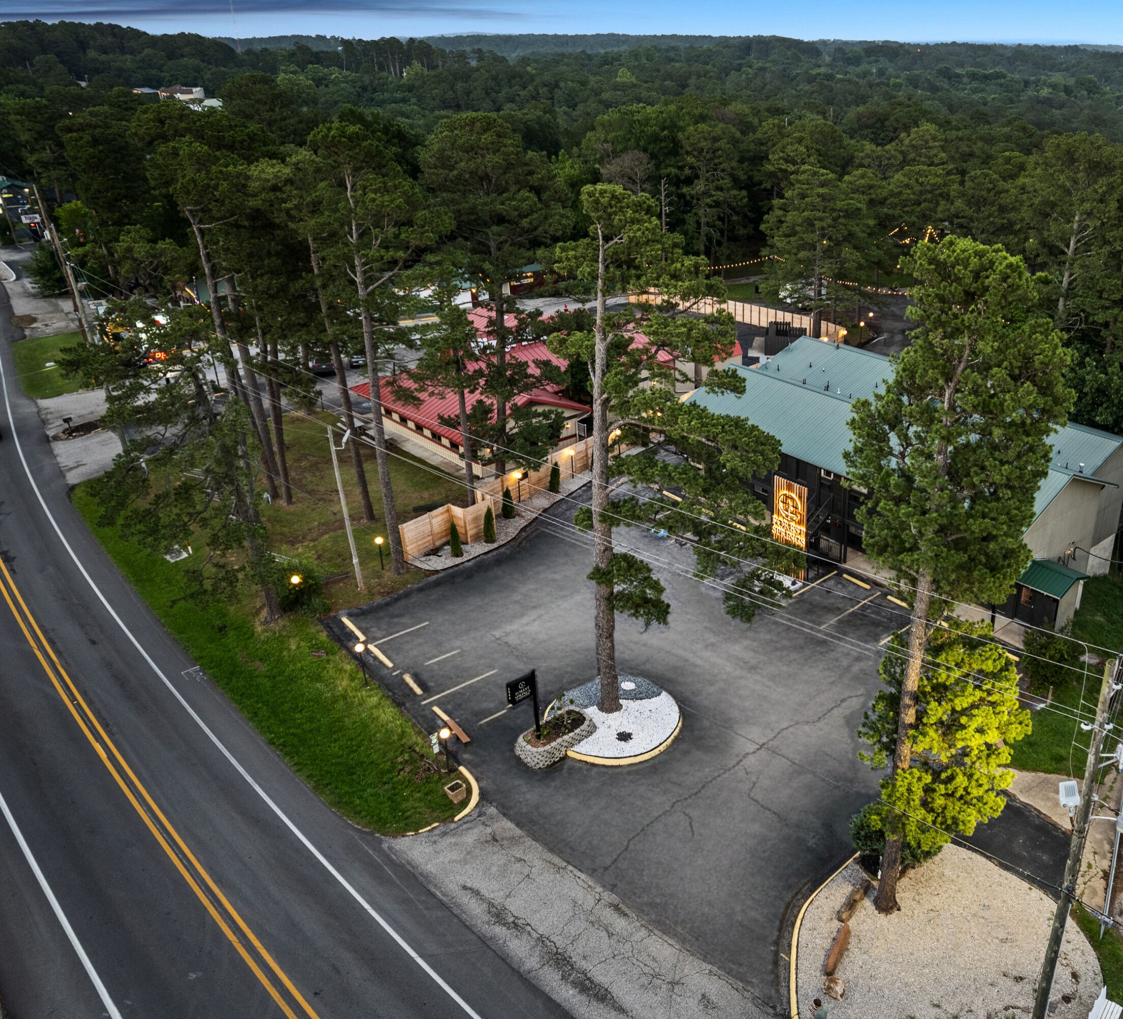 An aerial view of a parking lot with a central circular area, surrounded by trees and buildings with green roofs.