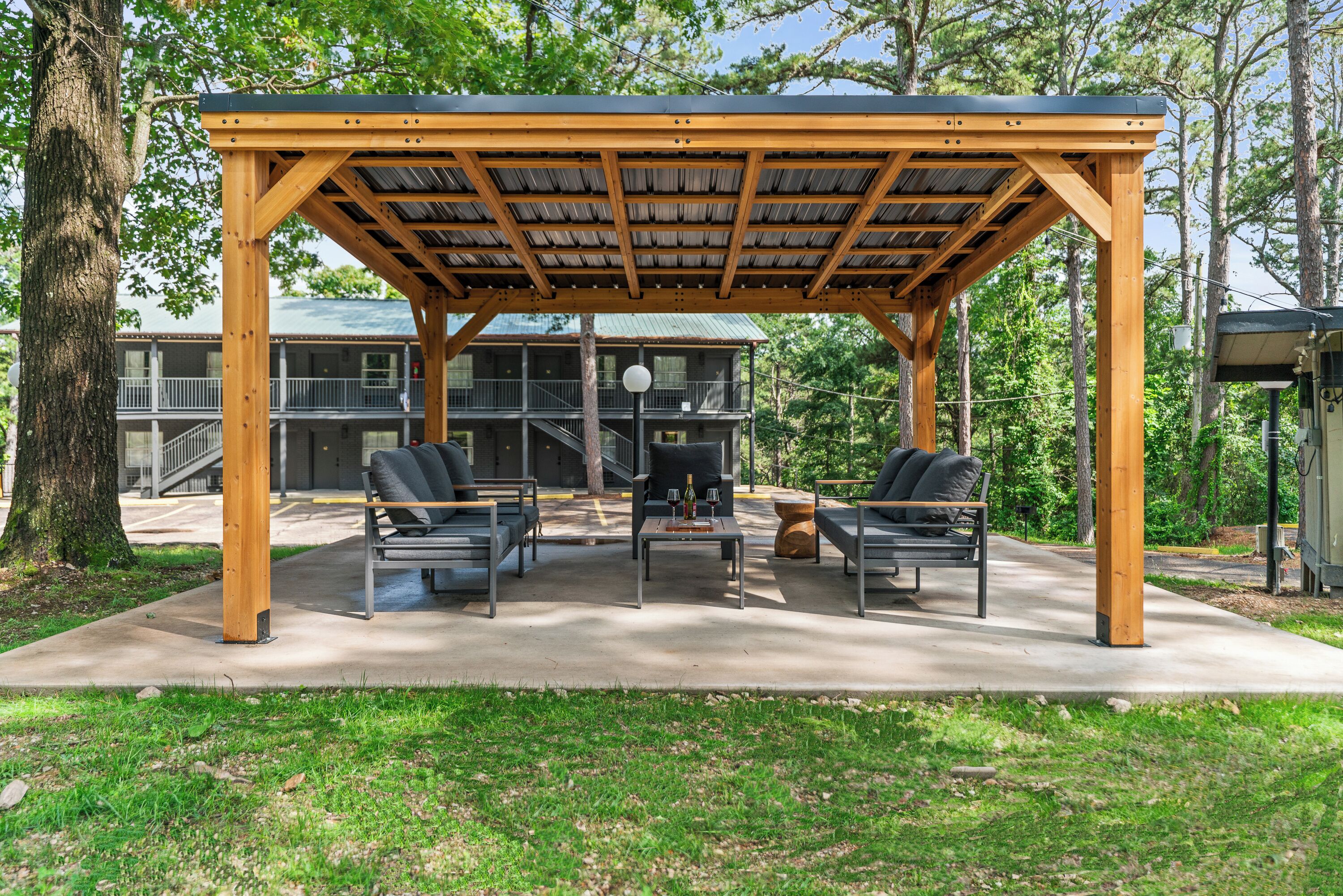 A covered outdoor seating area with a wooden structure, two tables, and four chairs.