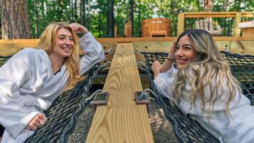 Duas pessoas relaxando em uma rede com estrutura de madeira e ambiente rústico.