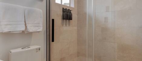A modern bathroom with a glass-enclosed shower, a toilet, and a window above the sink.