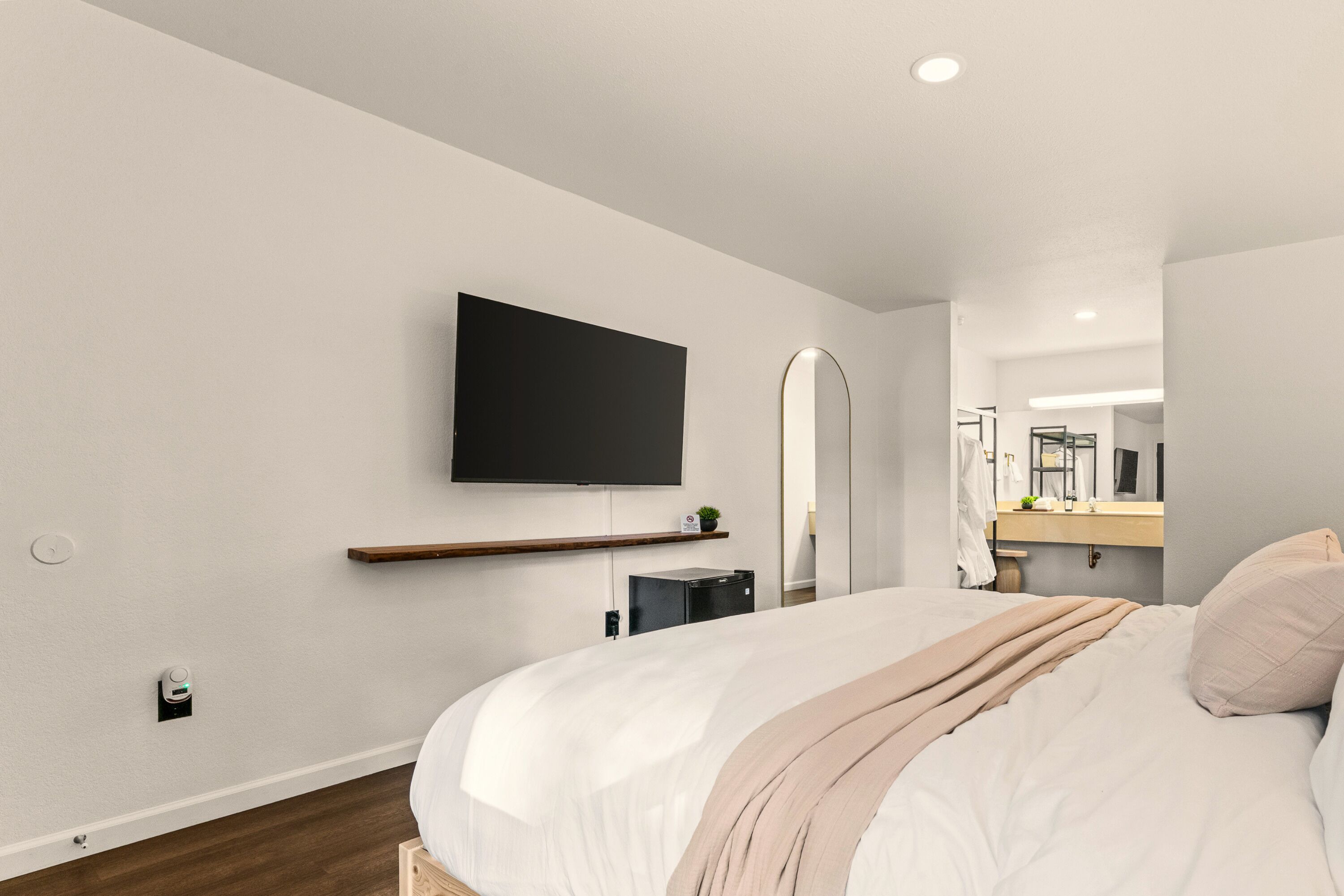 A modern bedroom with a bed, a mounted TV, a bedside table, and a mirror.