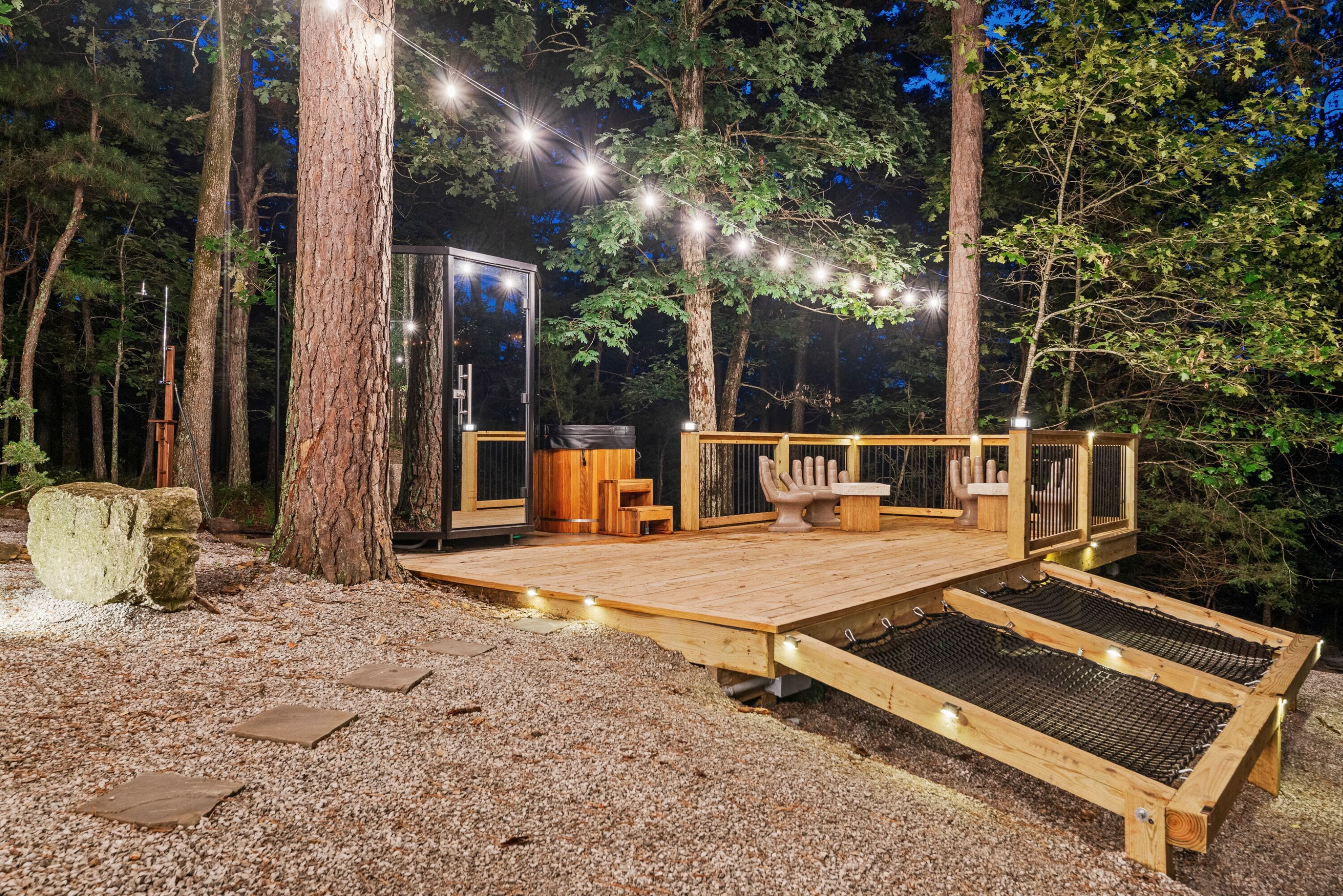 A wooden deck with a glass enclosure, string lights, and a bench.