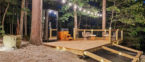 A wooden deck with a glass enclosure, string lights, and a bench.