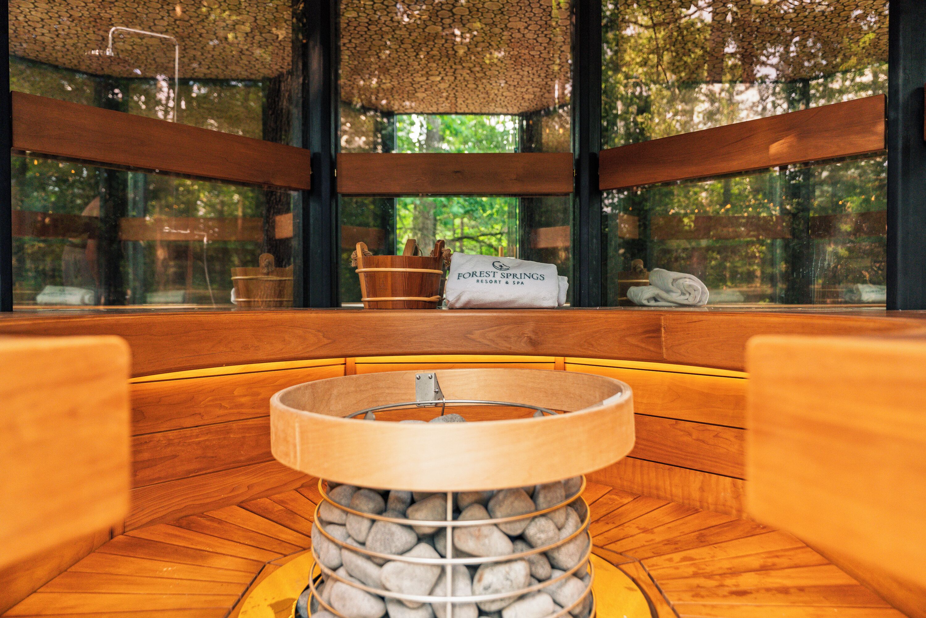 A wooden bench seating area with a central fire pit, a wooden bucket, and a towel on a bench.