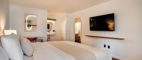 Un dormitorio moderno con una cama grande, un televisor montado en la pared y un escritorio con una silla.