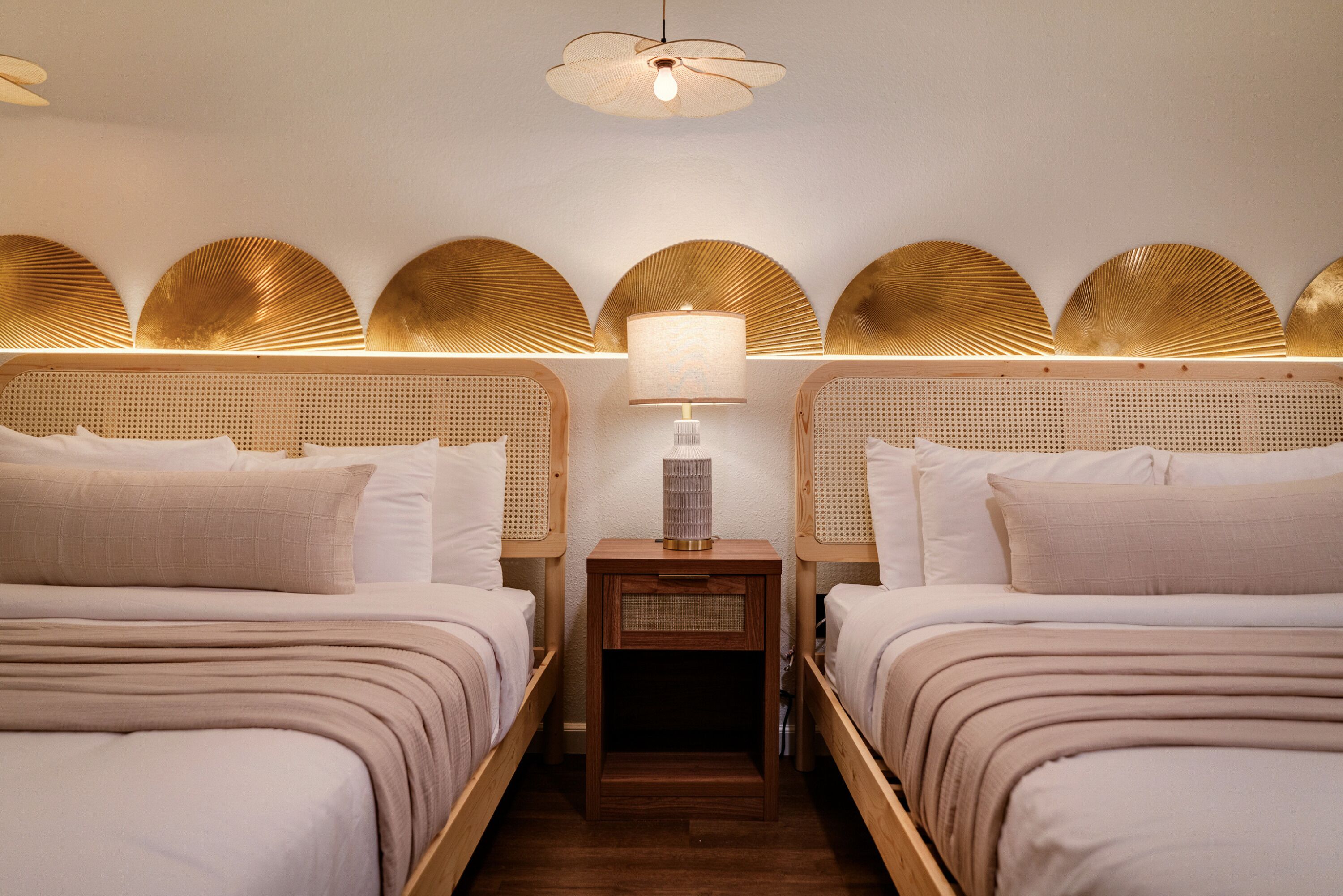 A hotel room with two beds, a nightstand with a lamp, and decorative wall panels.
