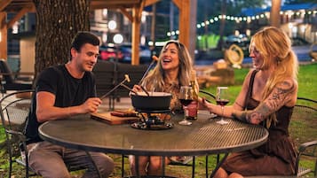 Three people dining outdoors at a round metal table with a pot and wine glasses.