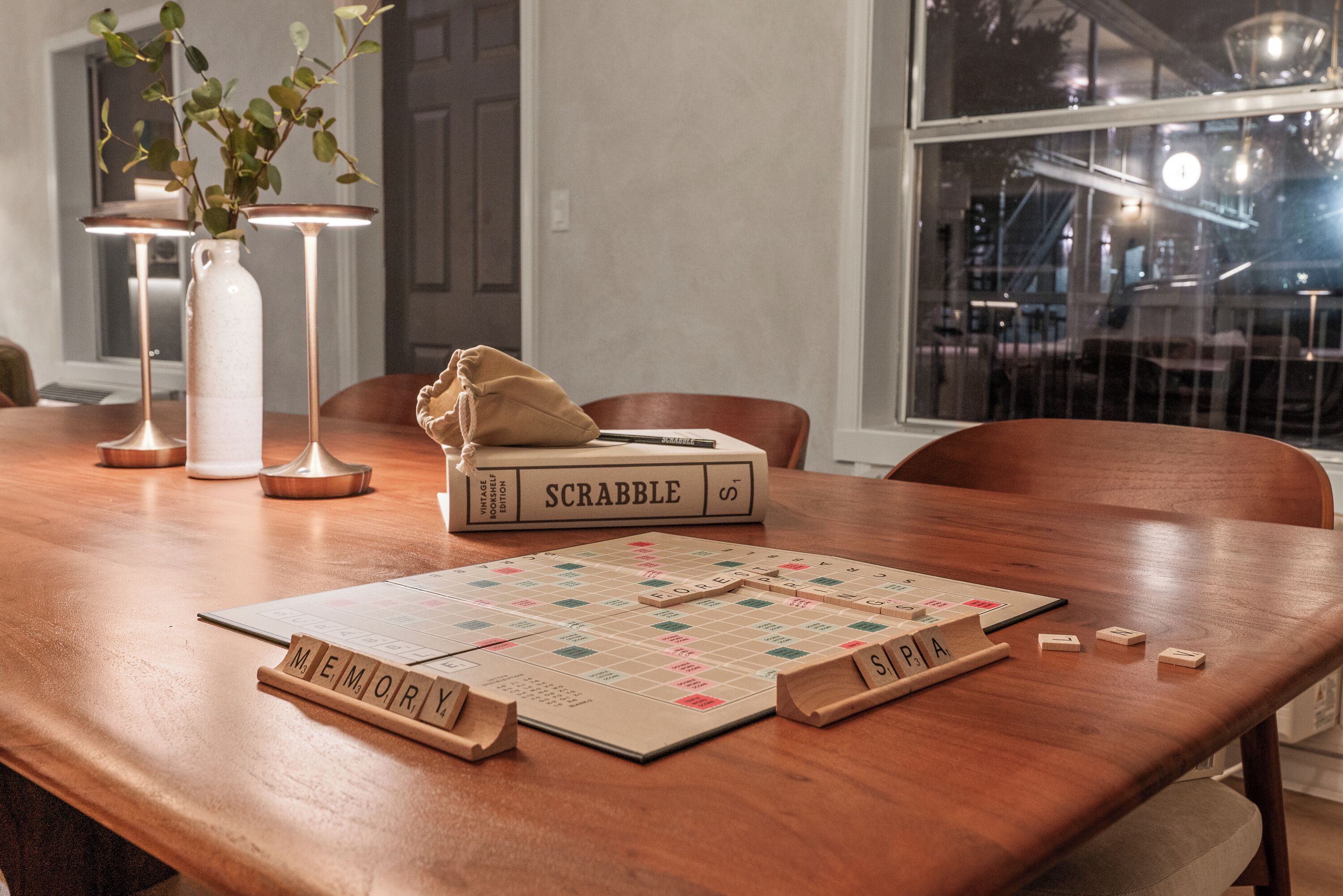 A wooden table with a Scrabble board, a book titled 'SCRABBLE,' and wooden letter tiles.