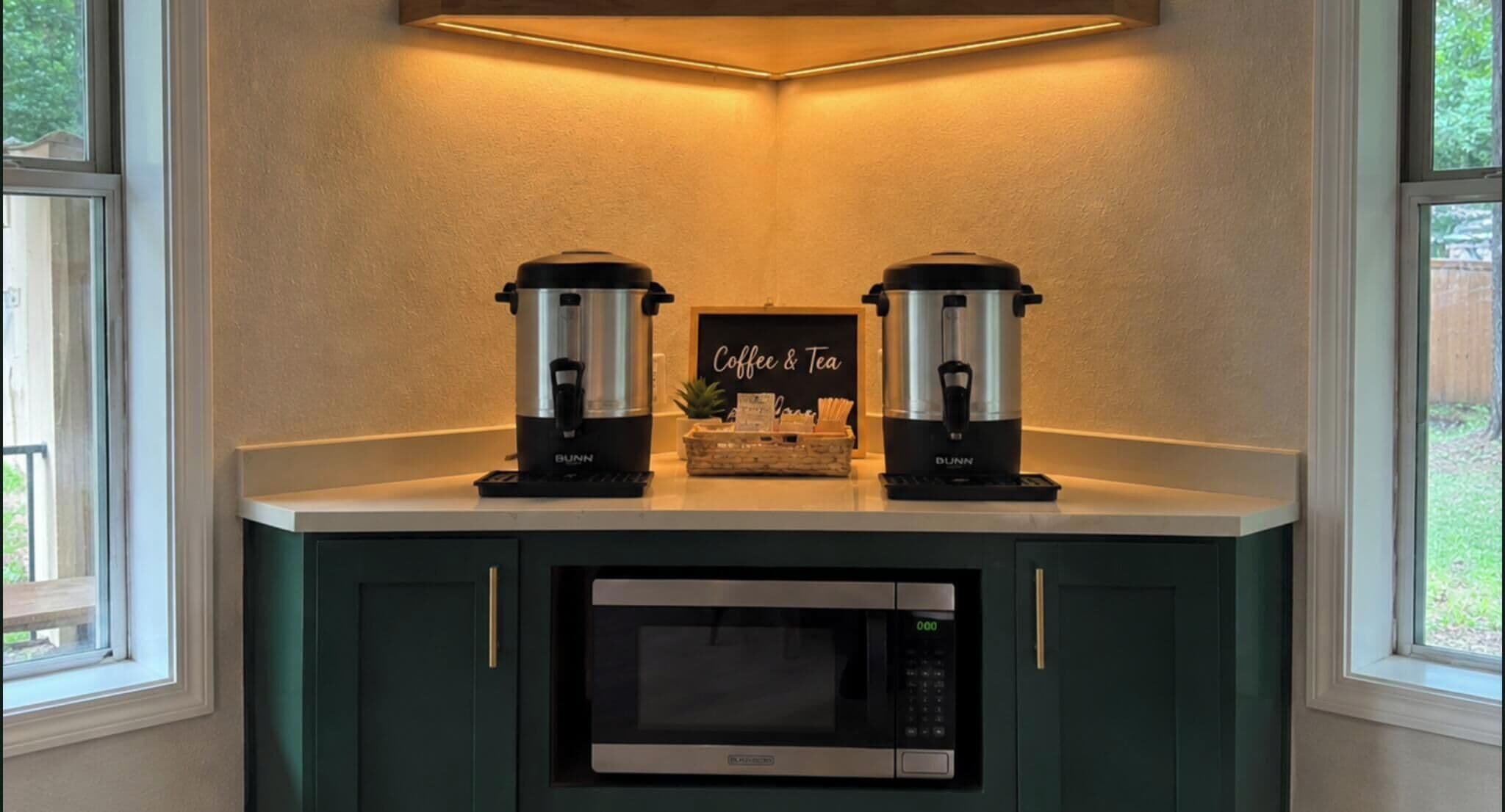 Eine Küchenzeile mit zwei Kaffeemaschinen, einer Mikrowelle und einem Schild mit der Aufschrift 'Coffee & Tea'.