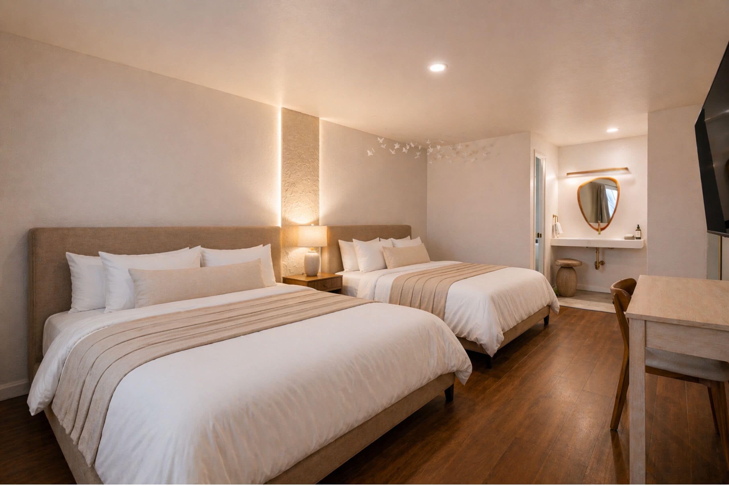 A hotel room with two beds, a small table, a chair, a TV, and a mirror on the wall.