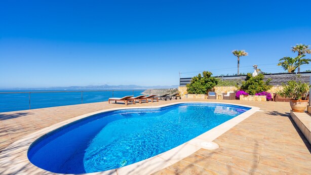A swimming pool with lounge chairs, a stone wall, and a view of the sea. - Sa Torre Voramar - with private swimming pool (LLucmajor)