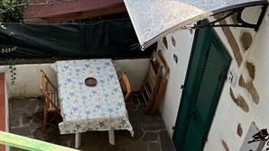Un'area salotto all'aperto coperta, con tavolo e sedie, una scala con ringhiera verde e pavimento in pietra.