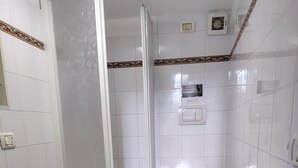 Un bagno con doccia, toilette, bidet e uno scaffale con articoli da toilette.