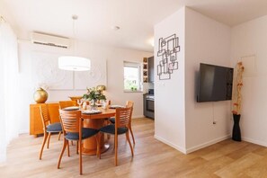 Ein modernes Wohnzimmer mit Essbereich, einem an der Wand befestigten Flachbildfernseher und einer Küche im Hintergrund.