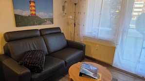 Ein Wohnzimmer mit einer schwarzen Ledersofa, einem runden Couchtisch, einem Gemälde eines Leuchtturms und einem Fenster mit Blick auf Gebäude.