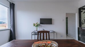 Un coin repas avec une table en bois, une chaise, un vase de fleurs et un téléviseur à écran plat fixé au mur.