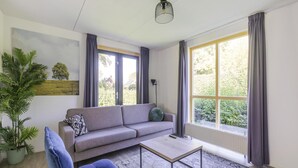 Una sala de estar moderna con un sofá, una mesa de centro, una silla, una lámpara de pie y un ventanal con cortinas.