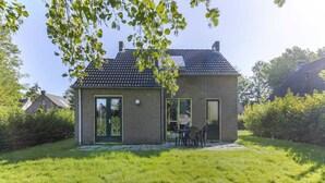 Una pequeña casa de ladrillo con techo de tejas, puerta de cristal y un patio con sillas.