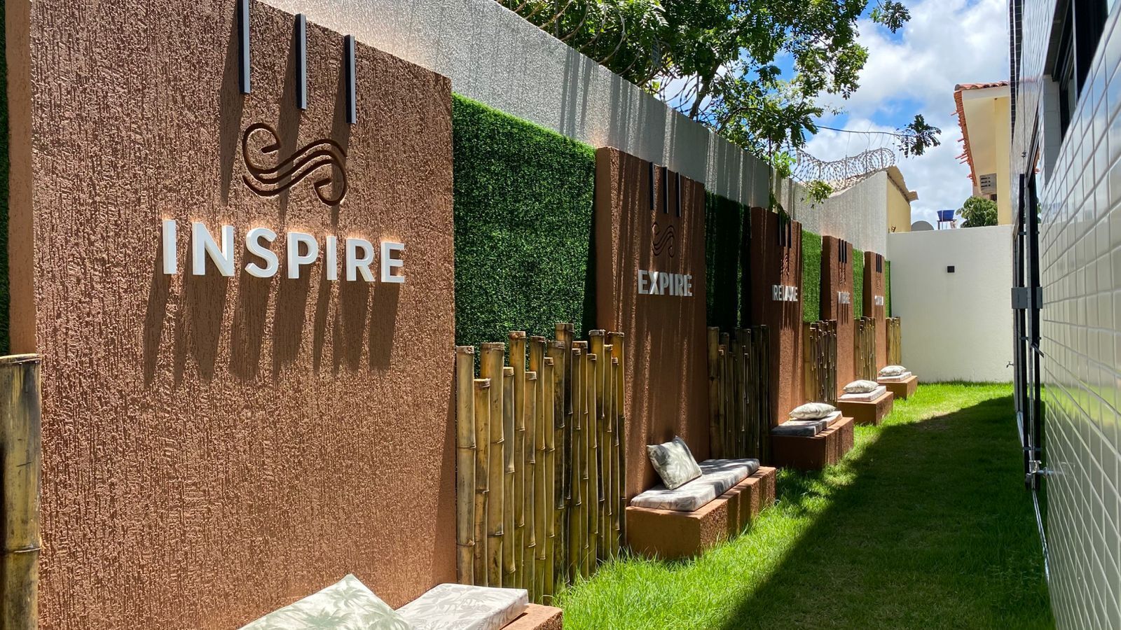 A spa area with a textured wall, a sign reading 'INSPIR', and a row of wooden benches with cushions.