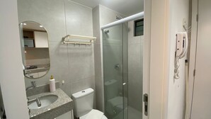 Egy modern fürőszoba üveg válaszfallal ellátott zuhanyzóval, mosdókagylóval, pulttal, WC-vel és tükörrel.