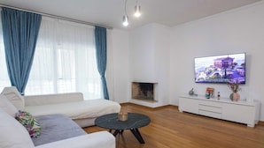 A living room with a sofa, a round coffee table, a fireplace, a TV on the wall, and a blue curtain. - Bright Minimal 2 Bd Apt in Marousi (Marousi)