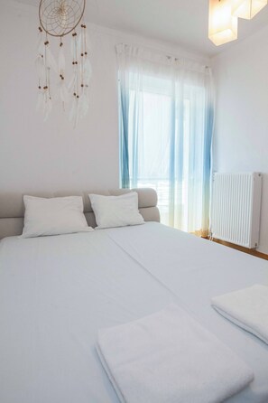 Une chambre avec un grand lit, du linge de lit blanc, un attrape-rêves et un radiateur.