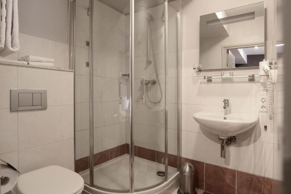 Un baño moderno con ducha envuelta en vidrio, un lavamanos blanco y un espejo sobre él.