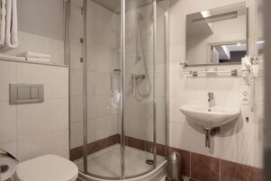 Un baño moderno con ducha envuelta en vidrio, un lavamanos blanco y un espejo sobre él.