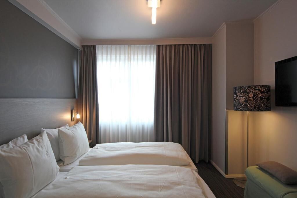 A hotel room with a large bed, a flat-screen TV, a bedside table, and a window with curtains.