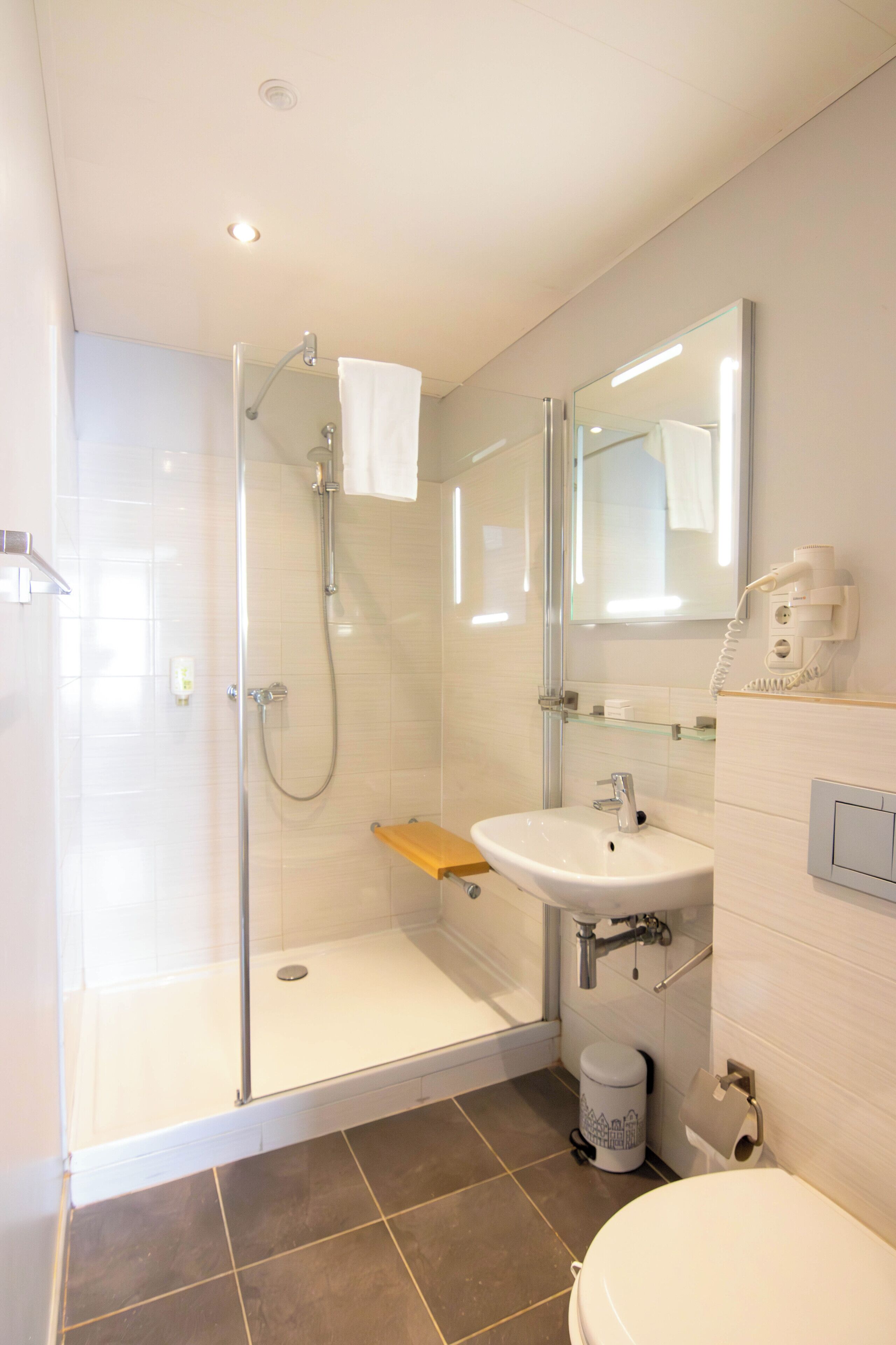 Een moderne badkamer met een douchecabine van glas, een wastafel met spiegel en een toilet.