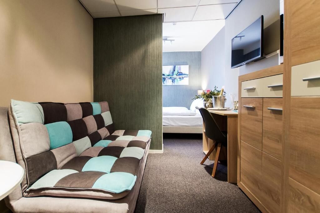 Quarto de hotel com sofá, escrivaninha, televisão e cama.