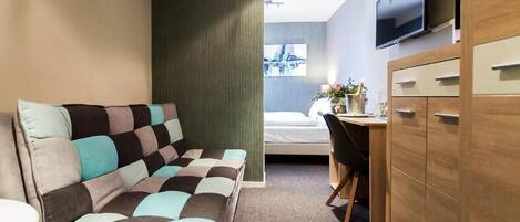 Quarto de hotel com sofá, escrivaninha, televisão e cama.