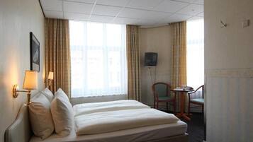 A hotel room with a bed, a desk, a chair, and a television.