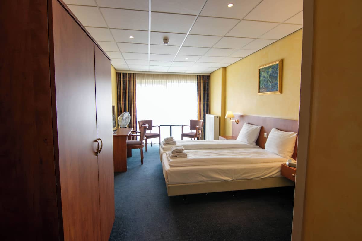 Habitación de hotel con una cama grande, un escritorio con silla, una lámpara de escritorio y un ventilador.