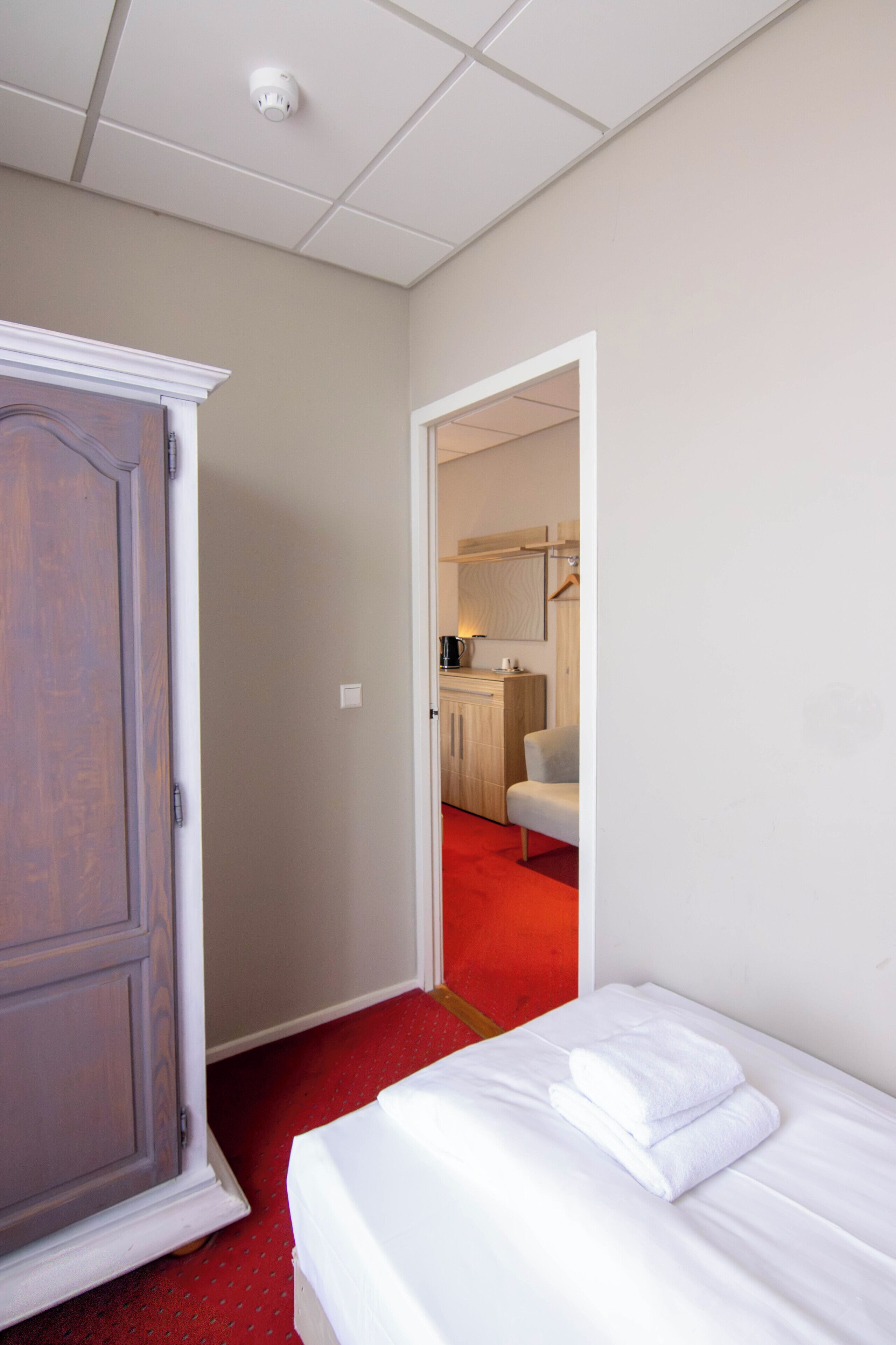 Una habitación de hotel con cama, armario, alfombra roja y vistas al área de la cocina.