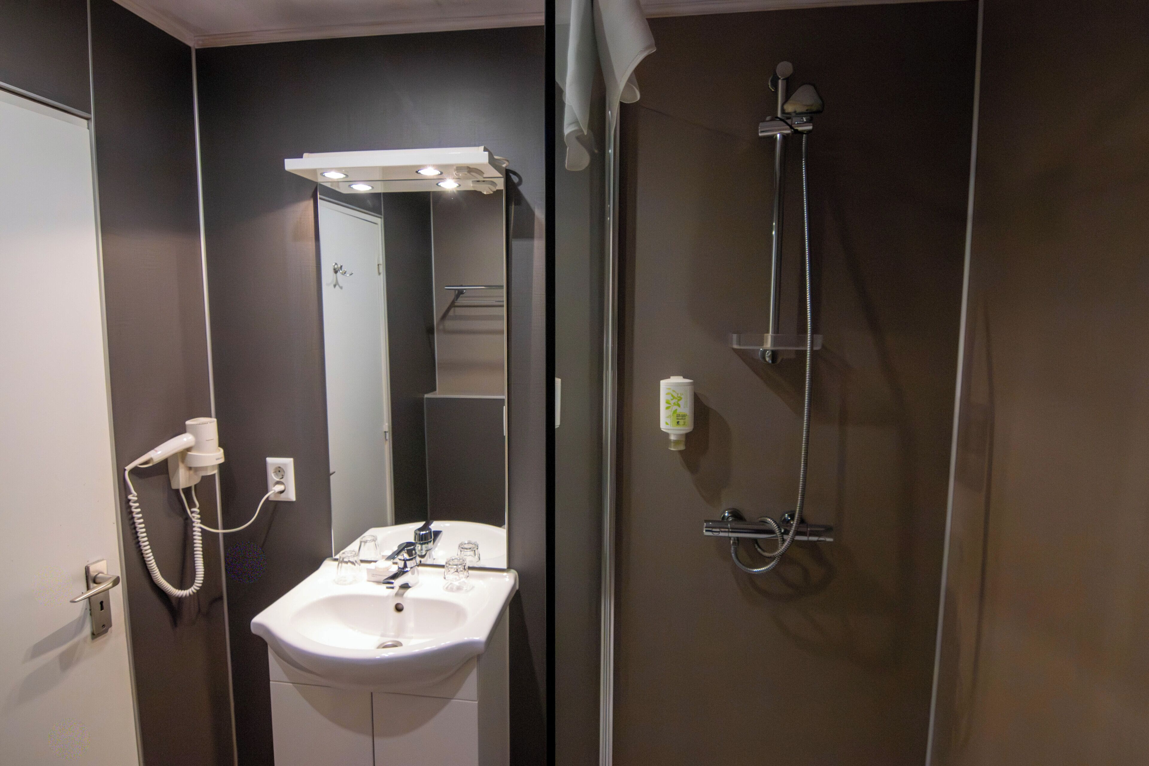 A bathroom with a sink, mirror, shower, and a hairdryer on the wall.