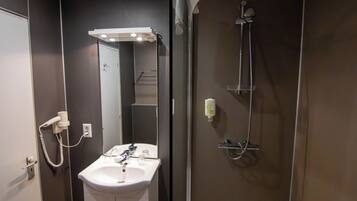 A bathroom with a sink, mirror, shower, and a hairdryer on the wall.