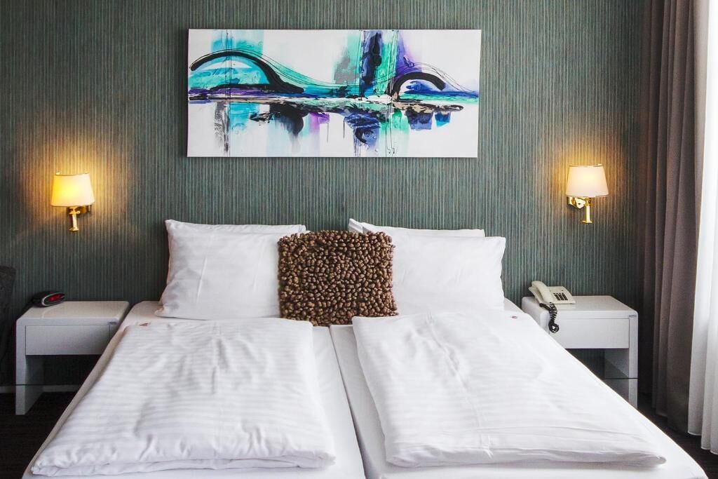 A hotel room with a bed, two bedside lamps, a painting on the wall, and a telephone on the nightstand.