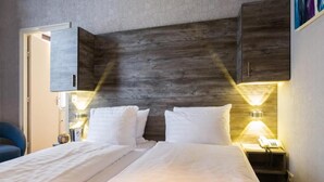 Una habitación de hotel con cama, lámparas de noche, un escritorio con teléfono y una silla.