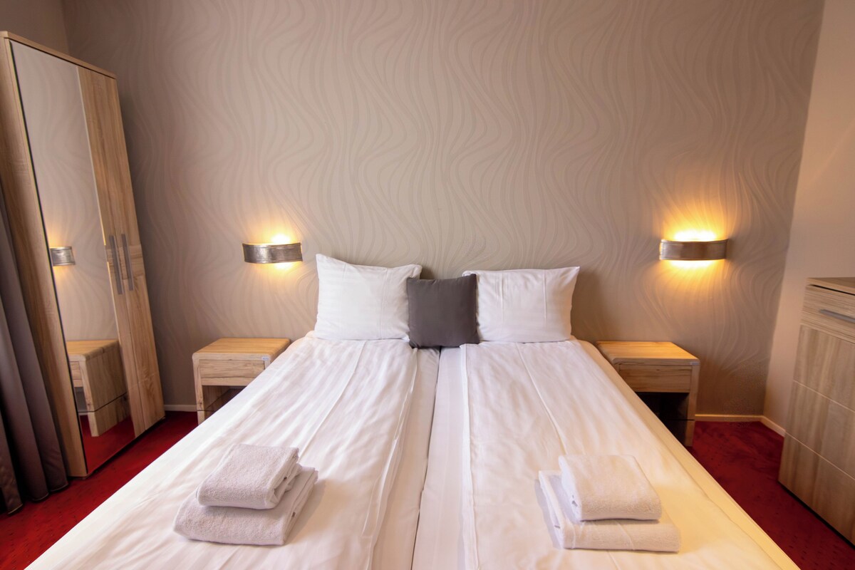 Una cama doble con ropa de cama blanca, dos mesitas de noche, un armario e iluminación en la pared.