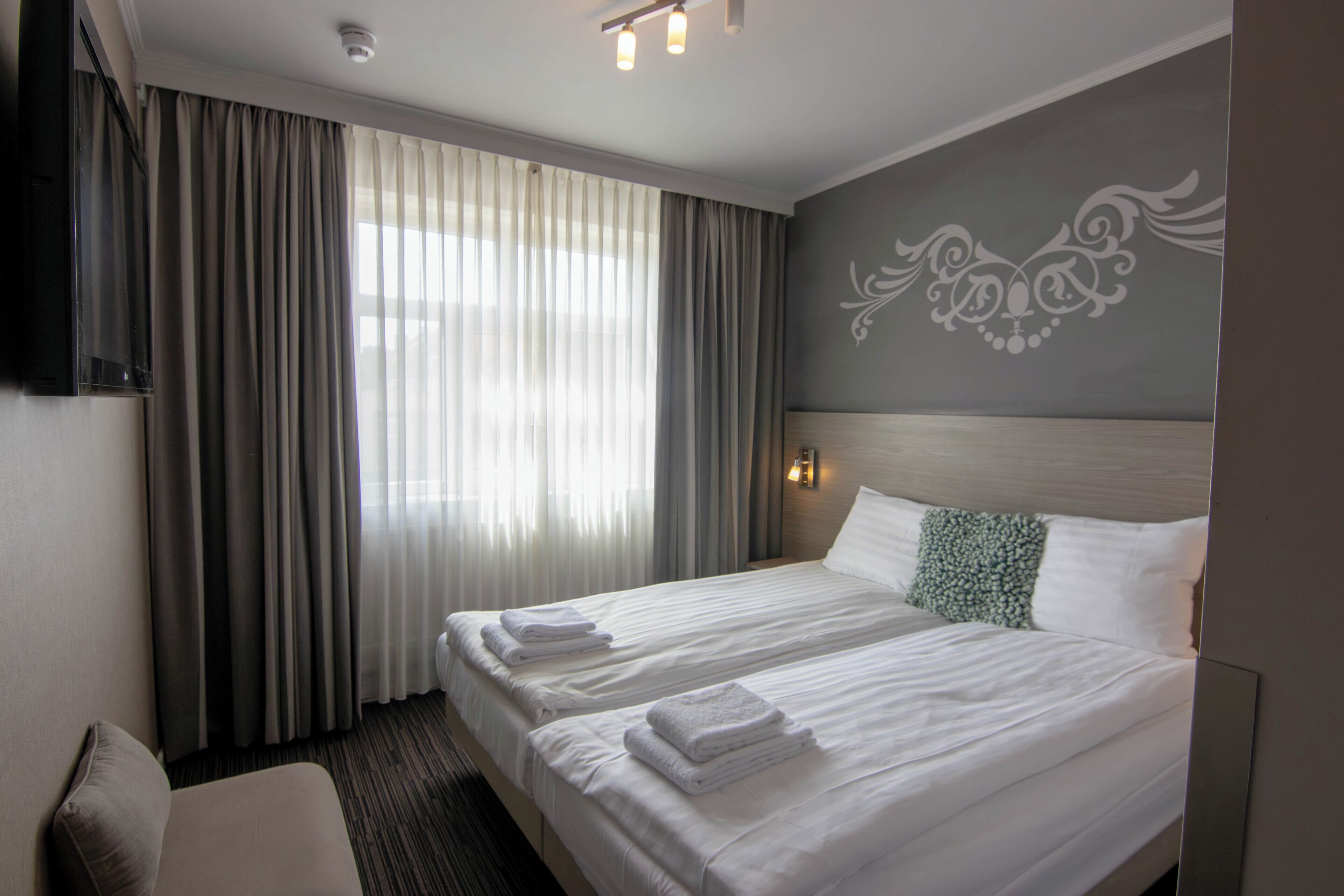 A hotel room with a large bed, a TV, and a window with curtains.