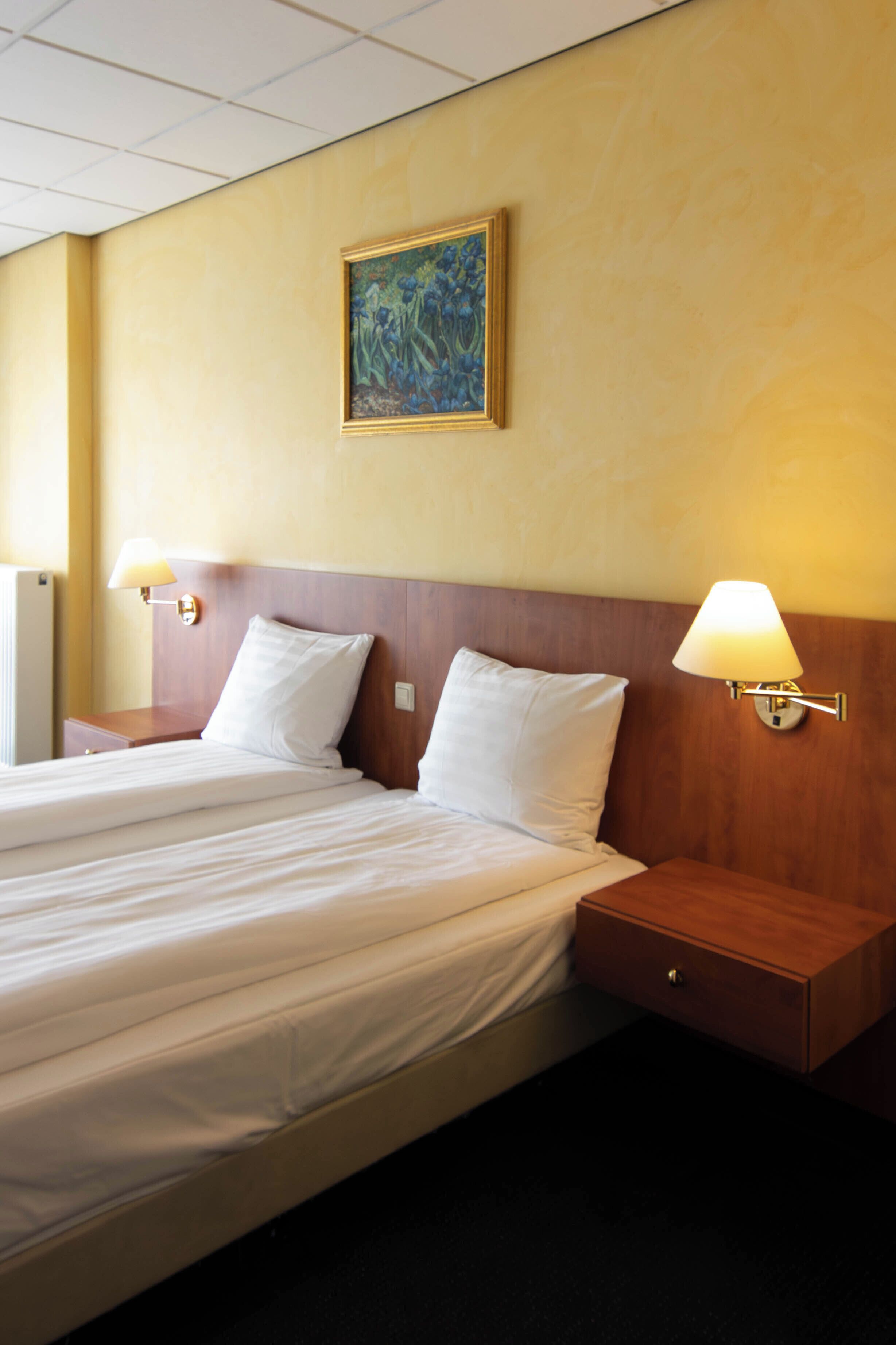 Ein Hotelzimmer mit einem großen Bett, zwei Nachttischlampen, einem Holzkopfschild, einem Nachttisch und einem Bild an der Wand.