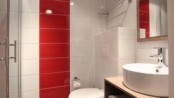 Een badkamer met een wit toilet, een wand betegeld met rode en witte tegels, een houten wastafelmeubel met een witte wastafel, en een spiegel boven de wastafel.