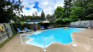 A rectangular swimming pool with a blue interior, surrounded by a concrete deck. There are two lounge chairs and a small umbrella near the pool. - Beautiful cottage located just steps from the main beach (Sauble Beach)