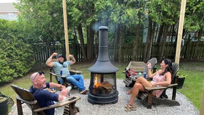 A patio with outdoor seating, a fire pit, and a wooden fence. - Beautiful cottage located just steps from the main beach (Sauble Beach)